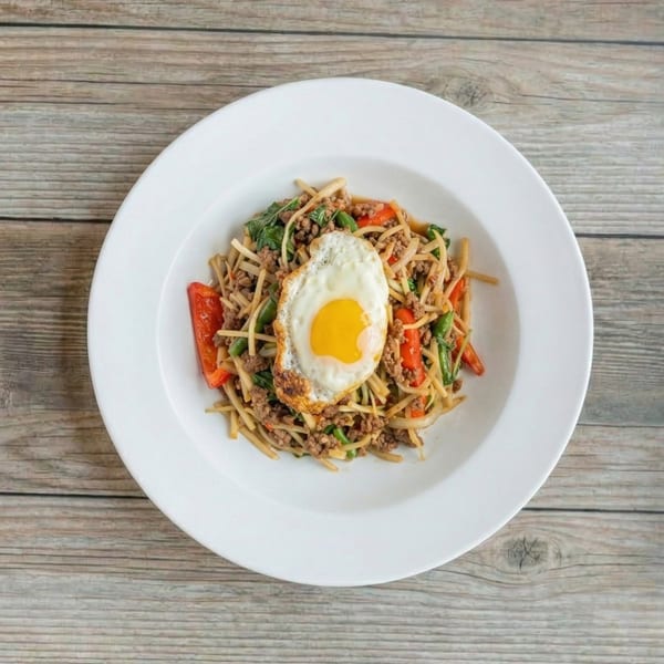 A white plate of Thai basil noodles with ground meat, vegetables, and a fried egg.