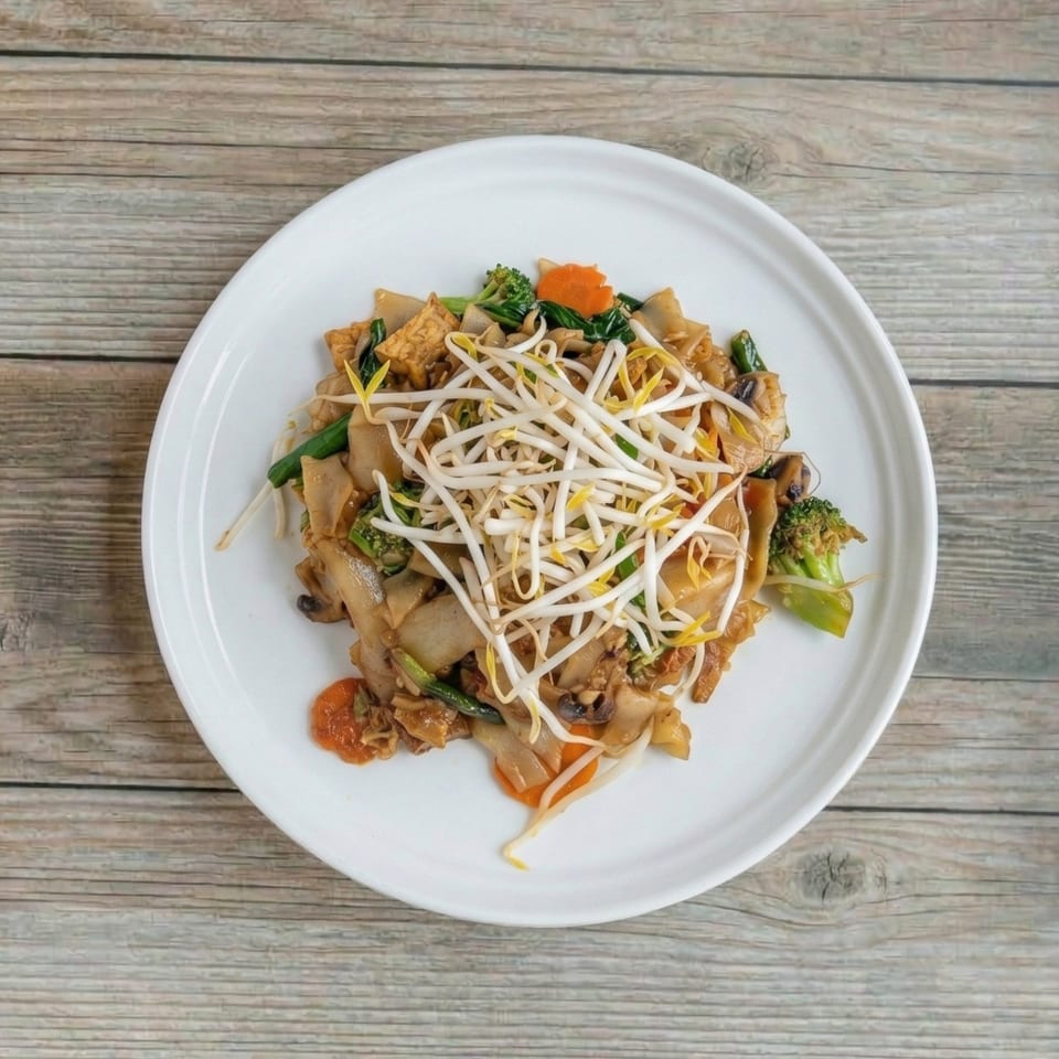 Pad See Ew with wide noodles, broccoli, carrots, tofu, and bean sprouts on a white plate.