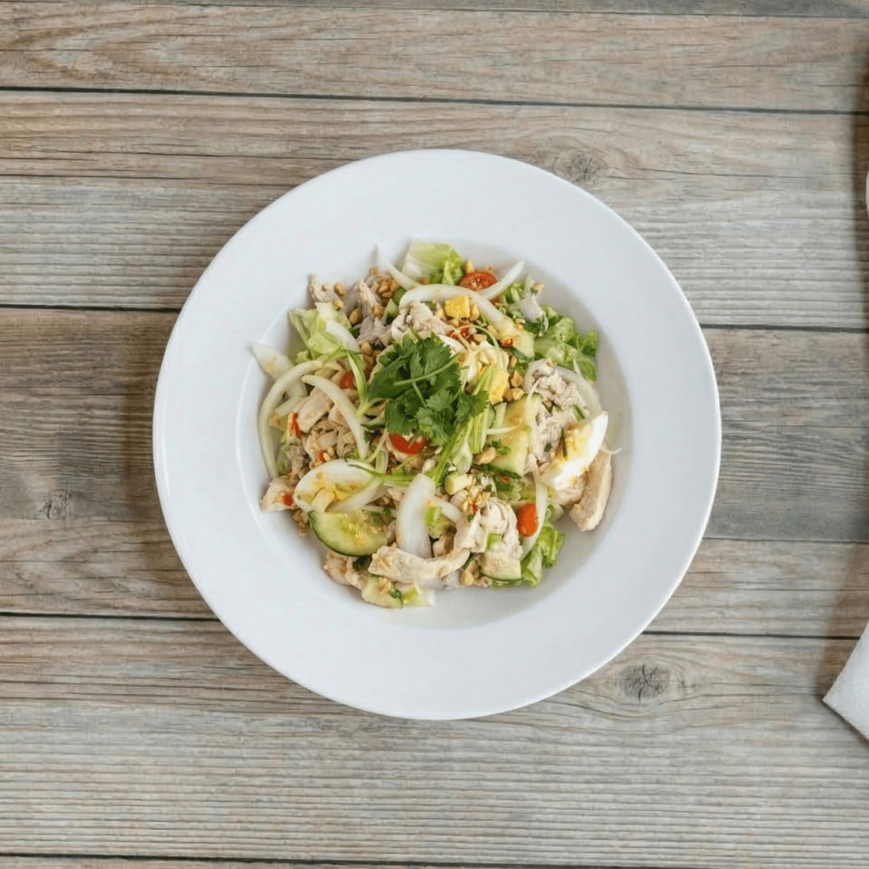 Overhead view of a chicken salad with lettuce, onions, cucumbers, tomatoes, and cilantro on a white plate.