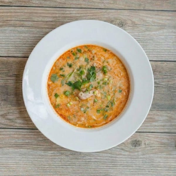 Overhead view of a white bowl filled with a creamy orange soup, garnished with green herbs.