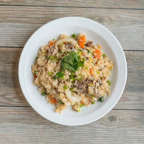 Beef fried rice with carrots, onions, and green onions, garnished with cilantro on a white plate.