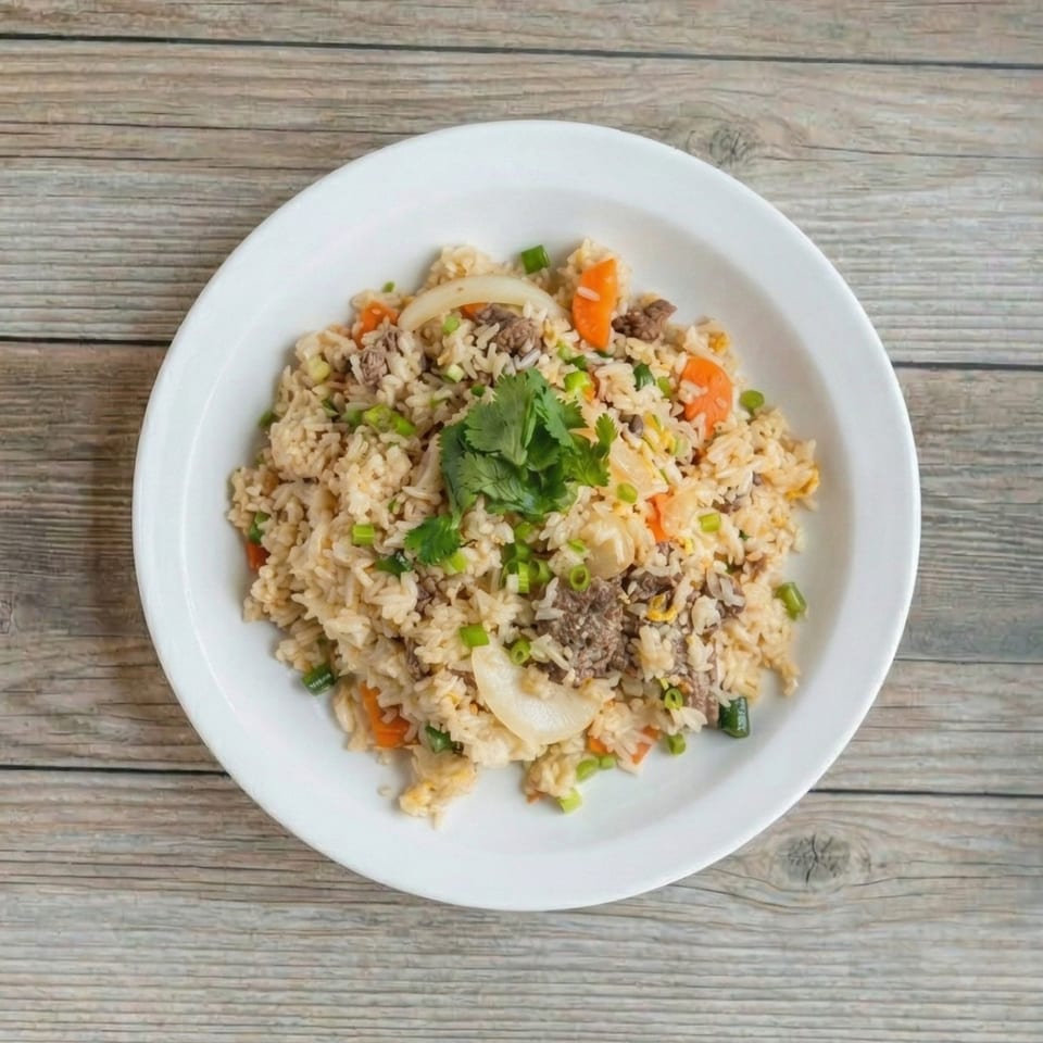Beef fried rice with carrots, onions, and green onions, garnished with cilantro on a white plate.