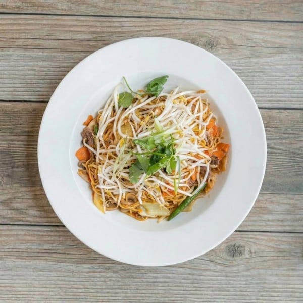 Overhead view of a white plate filled with stir-fried noodles, bean sprouts, vegetables, and cilantro.