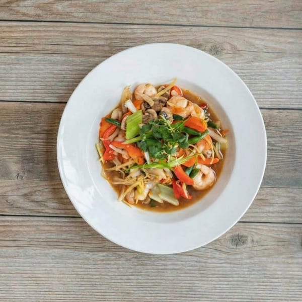 A white bowl of shrimp stir-fry with vegetables and mushrooms on a wooden table.