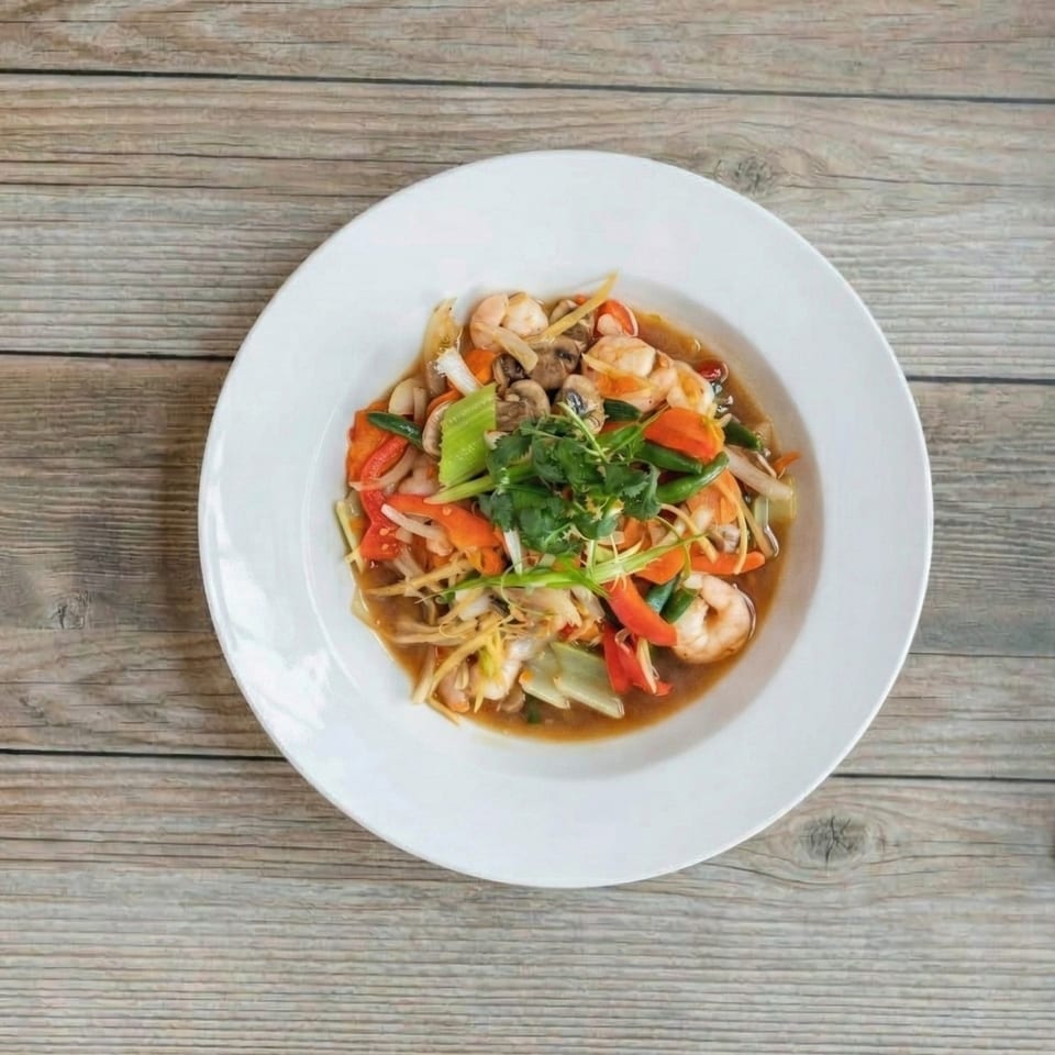 A white bowl of shrimp stir-fry with vegetables and mushrooms on a wooden table.